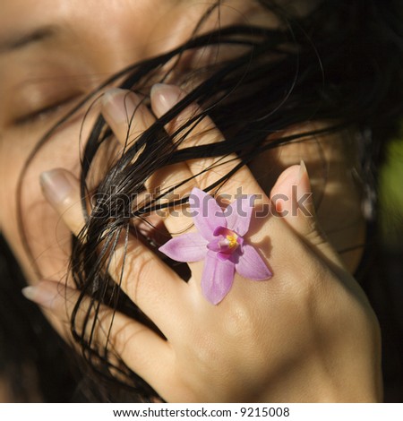 Mid-adult Asian female holding flower up to her face.