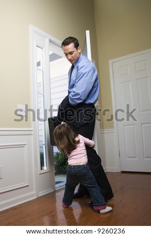 Caucasian businessman   at open door with briefcase with daughter tugging on his leg.