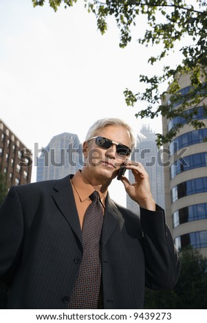 Caucasian middle aged businessman in sunglasses talking outdoors on cell phone.