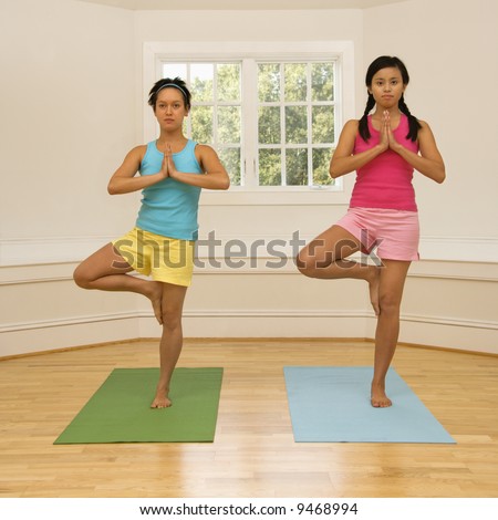 Two young women balancing doing yoga tree pose.