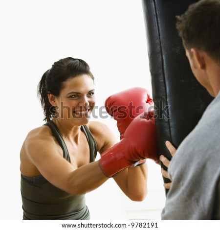 Woman wearing boxing gloves hitting training mits man is holding.