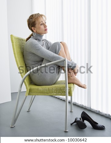 Pretty Caucasian woman sitting with legs curled up in chair looking away.