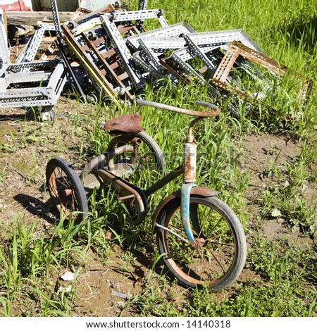 Old abandoned tricycle in grassy field next to junk pile