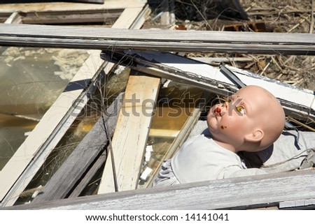 Old baby doll head sticking out of garbage at landfill.