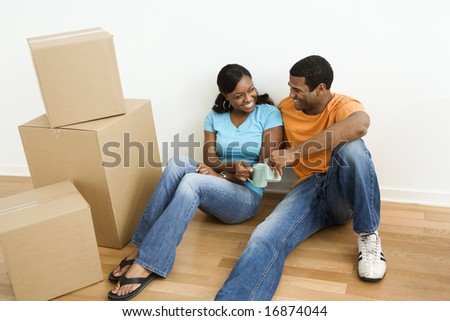 African American male and female couple sitting on floor next to moving boxes relaxing.