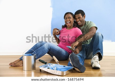 African American couple sitting together relaxing next to half-painted wall and painting supplies