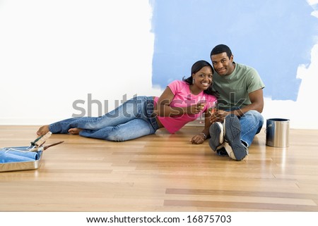 African American couple relaxing together with wine next to half-painted wall and painting supplies.