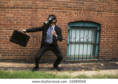 Businessman standing next to brick wall wearing gas mask in fighting stance.