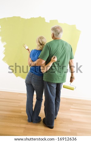 Middle-aged couple painting wall green observing their work.