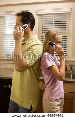 Father and daughter standing back to back talking on cell phones.  Vertically framed shot.
