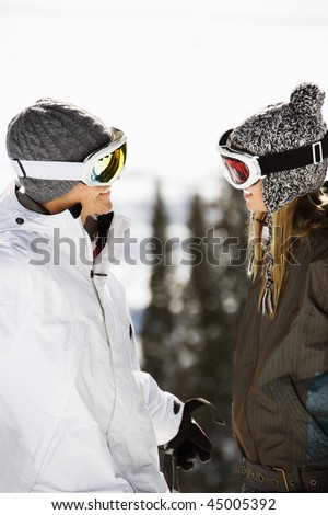 Skiers on a ski slope wearing ski goggles and hats and smiling at each other. Vertical shot.
