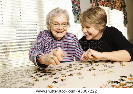 Elderly woman and a younger woman work on a jigsaw puzzle.  Horizontal shot.