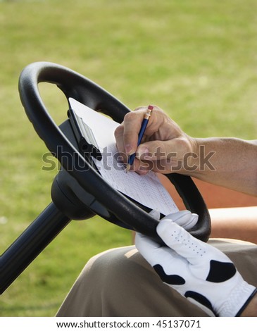 Male golfer writing his golf score while sitting in a golf cart. Vertical shot.