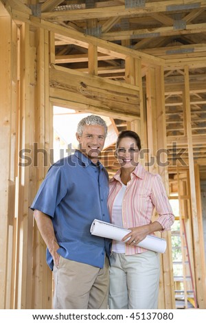 Happy couple stand together inside their home under construction. Vertical shot.
