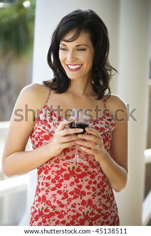 Portrait of happy woman standing and holding a glass of red wine. Vertical shot.