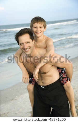 Father gives his son a piggy back ride at the beach. Vertical shot.