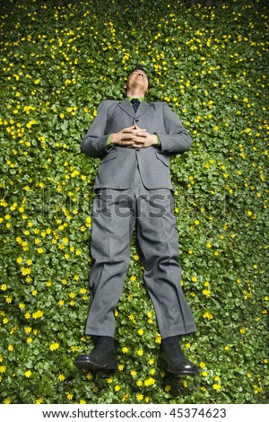 Young businessman relaxing in a bed of flowers and smiling with contentment. Vertical shot.