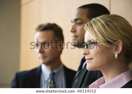 Close-up of Caucasian mid-adult businesswoman with two businessmen in background. Horizontal format.