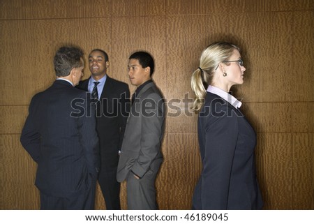 Businessmen of ethnic diversity talk in a group as a Caucasian businesswoman walks by. Horizontal shot.