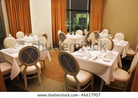 Empty seats in a restaurant dining area with a night time view shown through an open curtain in the background. Horizontal shot.