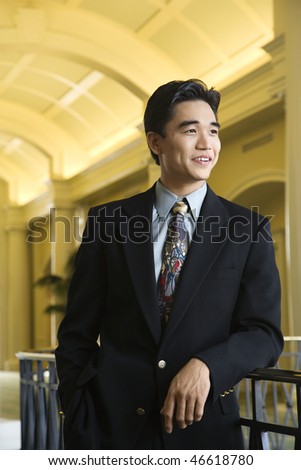 Portrait of an Asian businessman leaning on a rail in an upscale hotel. Vertical shot.