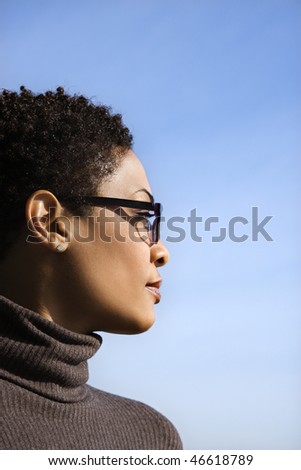 Attractive African American woman looks to the side against a blue sky background. Vertical shot.