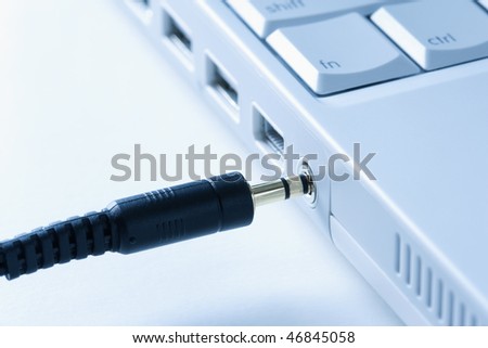Black headphone wire connecting to a laptop computer. Horizontal shot.