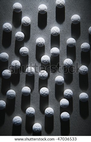 Close up of round white pills in a shaft of light, casting a shadow. Vertical shot.