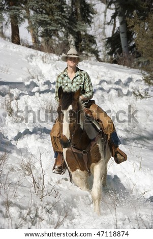 Attractive young woman riding a horse in the snow. Vertical shot.