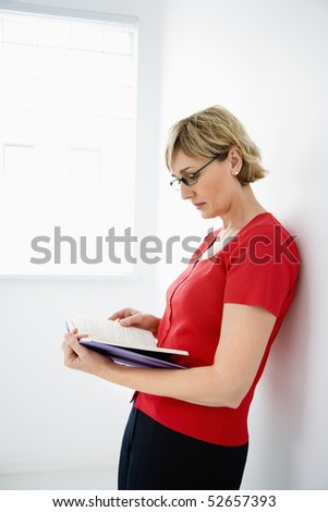 Woman standing wearing eyeglasses reading book.