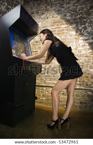 Attractive young woman standing wearing short dress playing video arcade game.