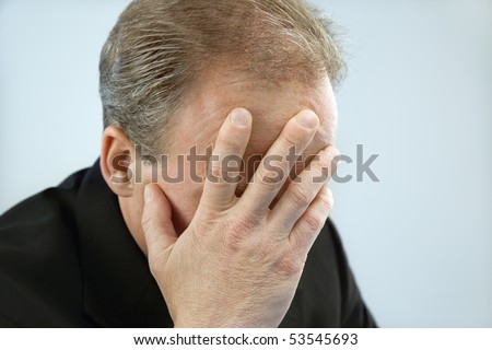 Head and shoulder portrait of middle aged  Caucasian businessman covering face with hand.