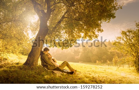 Loving couple under a big tree in the park in autumn