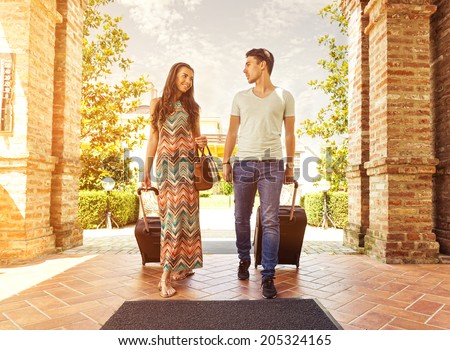 Young couple standing at hotel corridor upon arrival, looking for room, holding suitcases
