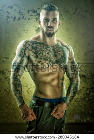 Tattoo, unique muscle-building man, standing in front of the wall