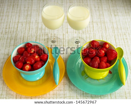 Strawberries in Yellow and Teal Bowls on Plates with Spoons and Milk