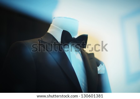 Black tuxedo suit on display behind shopping window glass.