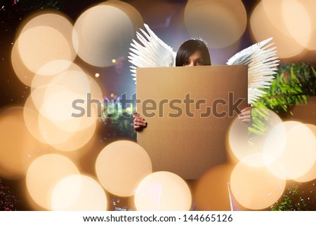 Angel woman with white wings holding blank cardboard message board poster over glowing golden lights background.
