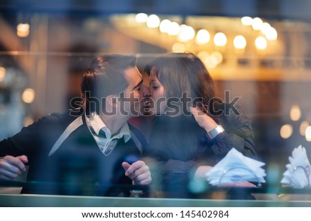 Romantic young valentine couple in love kissing in cafe. Candid view through window glass.