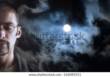 Man dreaming, eyes closed. Moon in cloudy sky background behind his face.