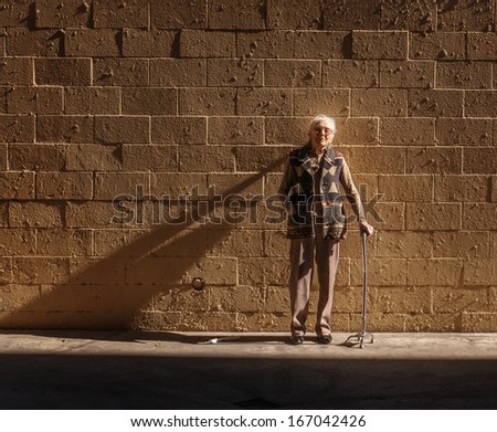 Portrait of senior woman standing near brick wall background. Copyspace.