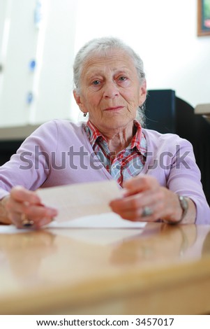 Portrait of a senior woman at home sitting at the table with papers. Shallow DOF.