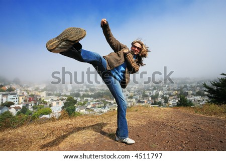 Young woman fooling around doing high kick ontop of the Kite Hill, San Francisco, California, USA.