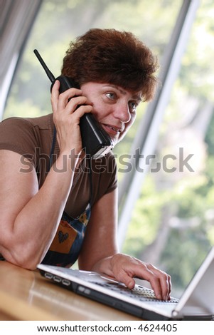 Mature woman at home talking on the phone with hand on laptop. Think \