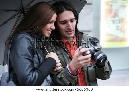 Young couple under umbrella, looking at digital SLR camera, smiling. Selective focus.