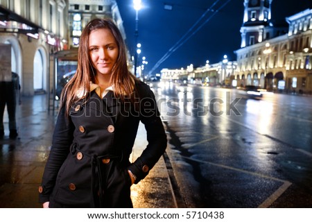 Beautiful young woman standing on illuminated street at night.