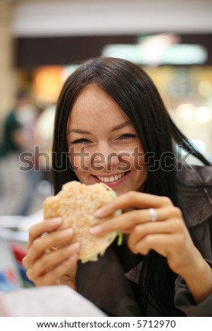 Beautiful girl eating hamburger and laughing. Shallow DOF.