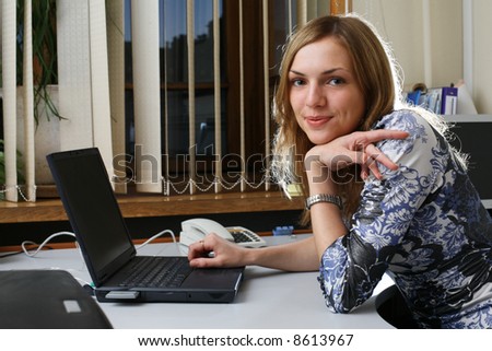 Young woman in office, laptop computer on table, looking in camera.