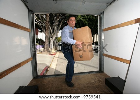 Man in blue shirt carrying cardboard boxes into empty truck.