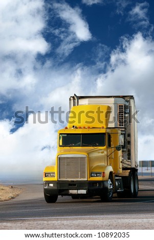 Big yellow trailer on the road over dramatic blue sky with white clouds.